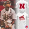 A Nebraska Cornhuskers baseball player celebrating next to the front and back views of a white and red team t-shirt.