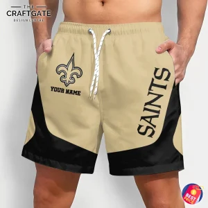A man models custom New Orleans Saints shorts from the front, featuring the team logo, a space for a name, and a gold and black design.